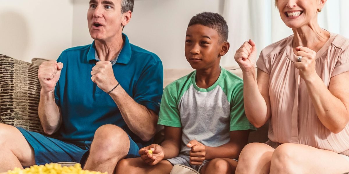 A family sharing laughs and popcorn during a cozy movie night at home, bridging generational entertainment gaps.